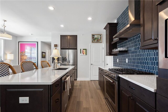 kitchen featuring appliances with stainless steel finishes, tasteful backsplash, hanging light fixtures, light hardwood / wood-style floors, and wall chimney exhaust hood