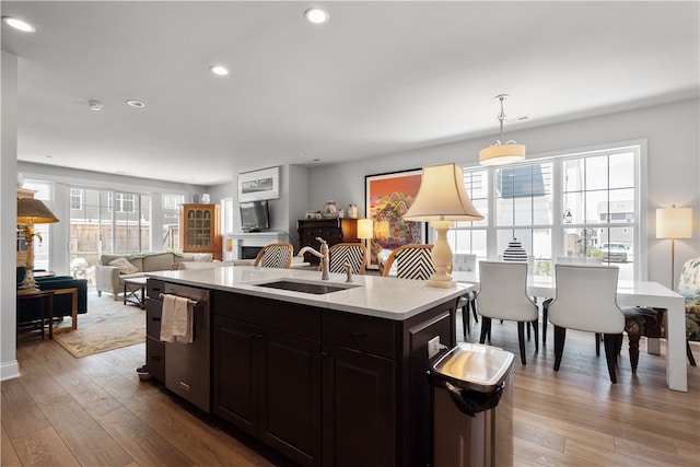 kitchen featuring light hardwood / wood-style flooring, sink, decorative light fixtures, stainless steel dishwasher, and a kitchen island with sink