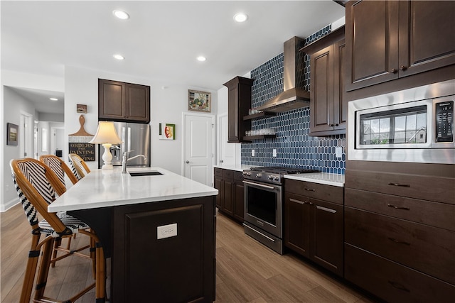 kitchen with wall chimney range hood, light wood-type flooring, sink, appliances with stainless steel finishes, and backsplash