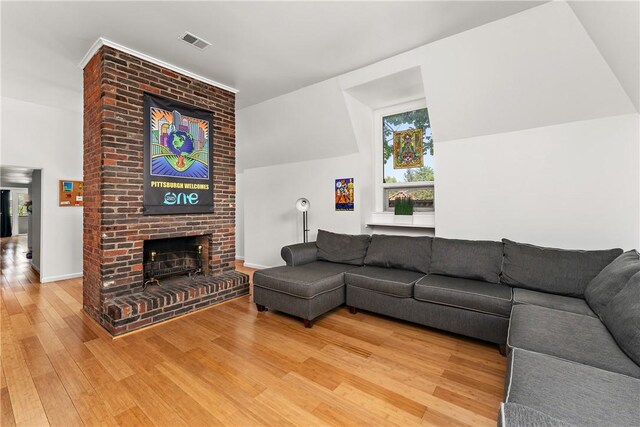 living room with brick wall, wood-type flooring, a brick fireplace, and vaulted ceiling