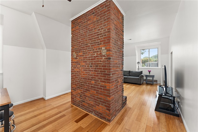 living room with lofted ceiling, light hardwood / wood-style floors, baseboard heating, and brick wall