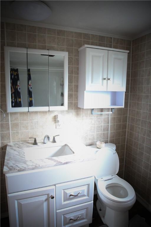 bathroom with tasteful backsplash, vanity, tile walls, and toilet