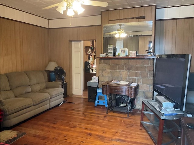 living area featuring wooden walls, ceiling fan, a wood stove, and hardwood / wood-style floors