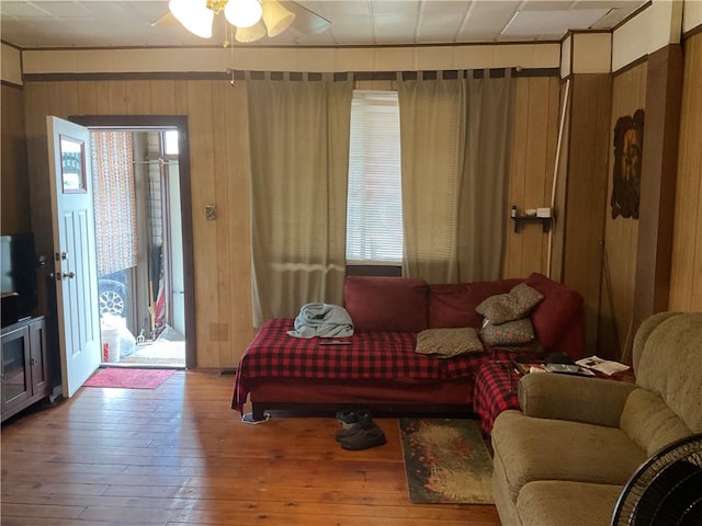 living room featuring wood-type flooring, wooden walls, and ceiling fan
