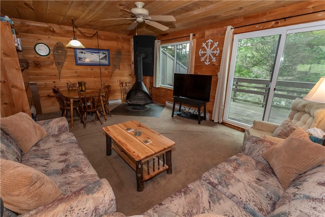 carpeted living room featuring ceiling fan, wood walls, a wood stove, and wood ceiling