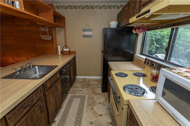 kitchen with dark brown cabinetry, wooden walls, sink, and black appliances