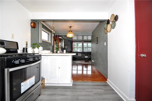 kitchen featuring stainless steel gas range oven, kitchen peninsula, decorative light fixtures, and dark hardwood / wood-style floors