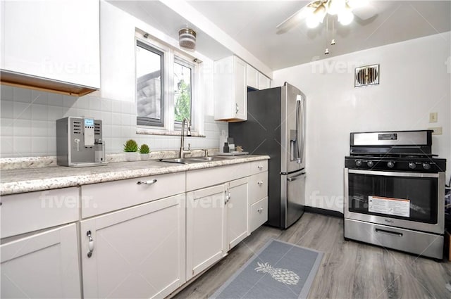 kitchen featuring white cabinetry, sink, tasteful backsplash, light hardwood / wood-style floors, and appliances with stainless steel finishes