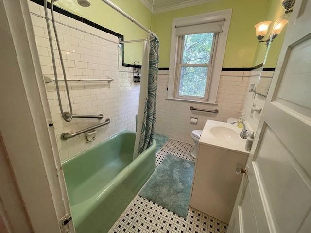 full bathroom featuring shower / tub combo with curtain, tile walls, ornamental molding, vanity, and toilet