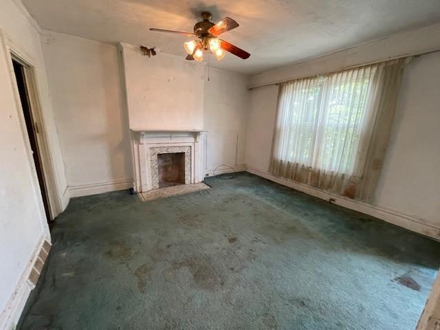 unfurnished living room with a premium fireplace, ceiling fan, and dark colored carpet