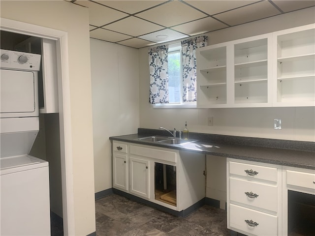 kitchen featuring sink, white cabinetry, stacked washer and clothes dryer, and a drop ceiling