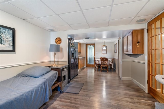 bedroom featuring dark hardwood / wood-style flooring, black fridge with ice dispenser, and a drop ceiling