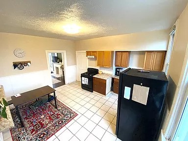 kitchen with black fridge, light tile patterned flooring, a textured ceiling, and stove