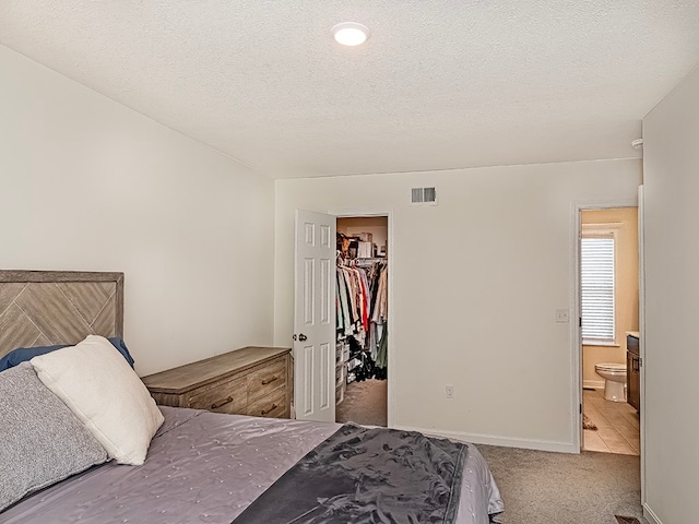 bedroom with a spacious closet, ensuite bathroom, a closet, carpet, and a textured ceiling