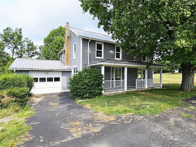 view of front of home featuring a chimney, aphalt driveway, metal roof, covered porch, and a front lawn