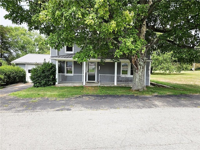 view of property hidden behind natural elements featuring a garage, metal roof, a porch, and a front yard