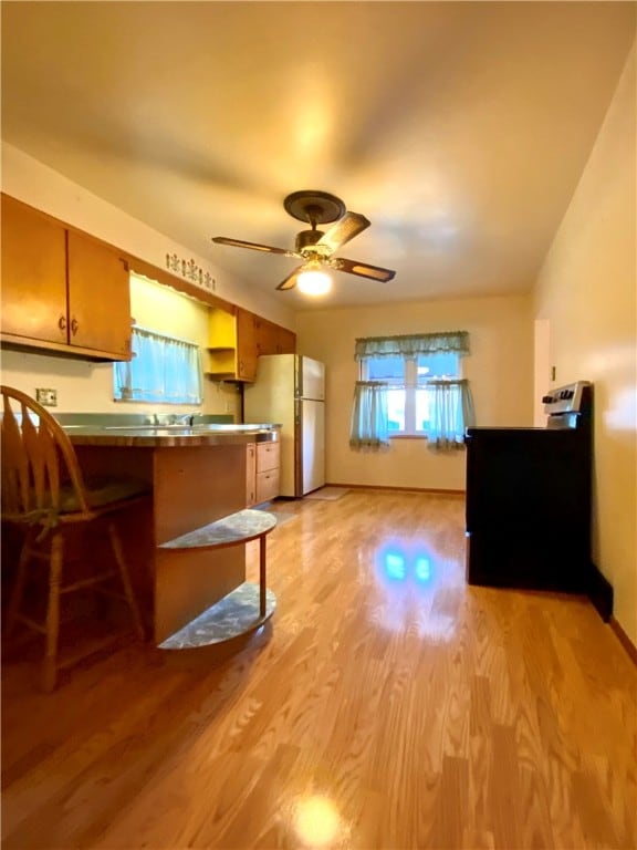 kitchen with a breakfast bar, kitchen peninsula, ceiling fan, white fridge, and light hardwood / wood-style flooring