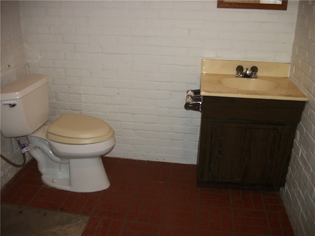 bathroom featuring brick wall, vanity, tile patterned flooring, and toilet