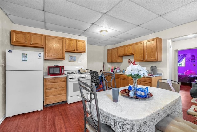 kitchen with dark wood-type flooring, white appliances, and a drop ceiling