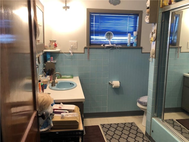 full bathroom with tile patterned floors, toilet, bath / shower combo with glass door, tile walls, and vanity