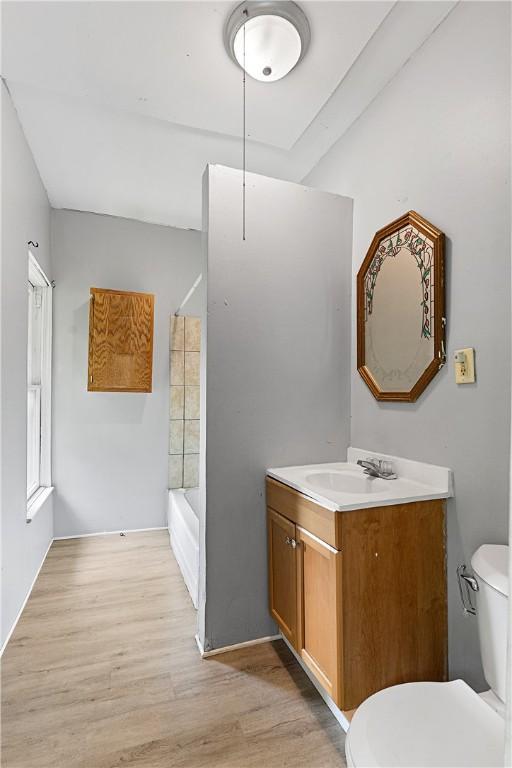 bathroom with washtub / shower combination, toilet, vanity, and wood finished floors