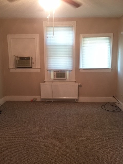 carpeted spare room with radiator, ceiling fan, and cooling unit