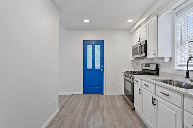 kitchen with white cabinetry, stainless steel appliances, sink, light stone counters, and light hardwood / wood-style floors