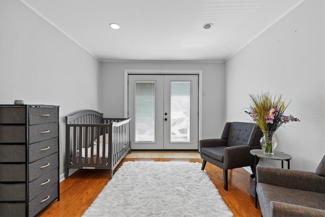 bedroom with a crib, wood-type flooring, and french doors