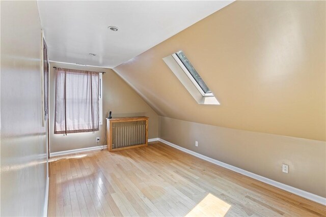 additional living space with light hardwood / wood-style flooring and vaulted ceiling with skylight