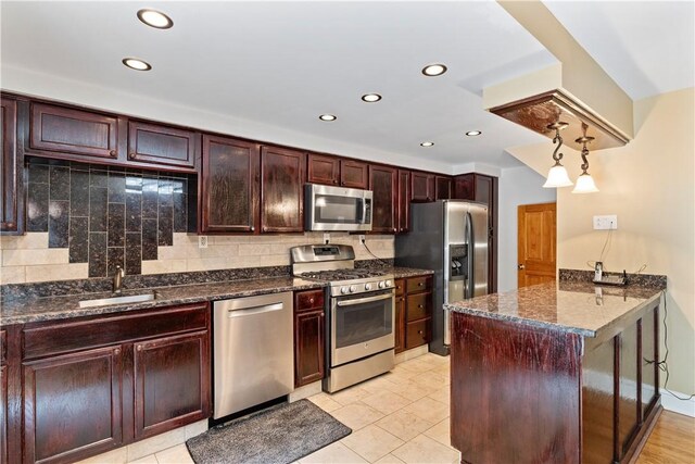 kitchen with dark stone counters, appliances with stainless steel finishes, decorative backsplash, decorative light fixtures, and sink