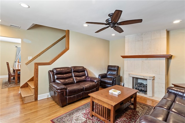 living room with a tiled fireplace, light wood-type flooring, ceiling fan, and tile walls