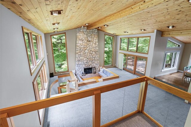 living room featuring wood-type flooring, wooden ceiling, a stone fireplace, and vaulted ceiling with beams