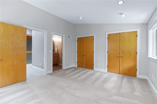 unfurnished bedroom featuring multiple closets, ensuite bathroom, light carpet, and lofted ceiling