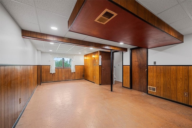 basement featuring wooden walls and a paneled ceiling