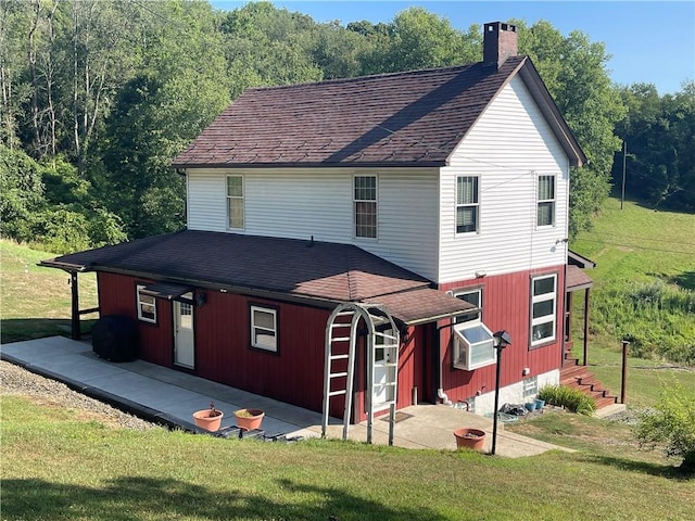 view of front of property featuring a patio area, roof with shingles, a chimney, and a front lawn