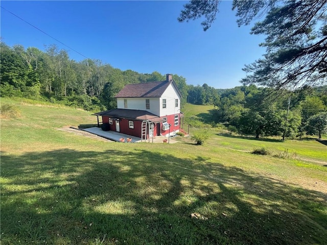 view of home's exterior featuring a forest view, a chimney, and a lawn