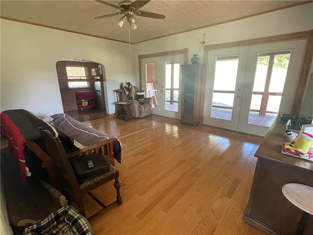 living area with ceiling fan, arched walkways, french doors, light wood finished floors, and ornamental molding