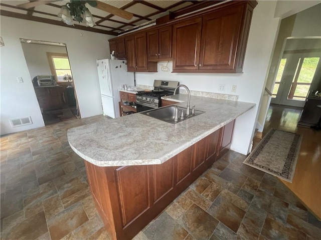 kitchen with stainless steel gas range oven, visible vents, a sink, stone tile flooring, and freestanding refrigerator