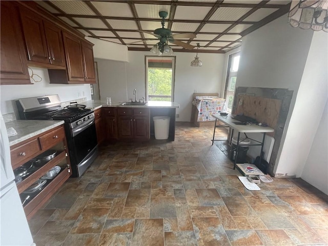kitchen featuring stainless steel range with gas cooktop, a ceiling fan, a sink, a peninsula, and stone finish floor