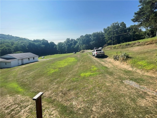 view of yard with a rural view, driveway, and a wooded view