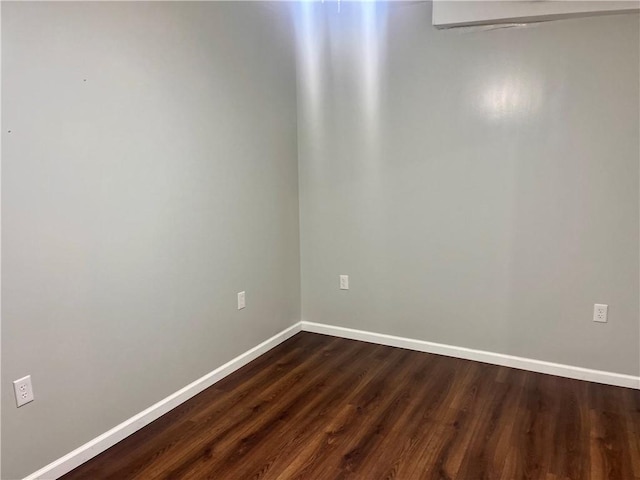 spare room with baseboards and dark wood-style flooring