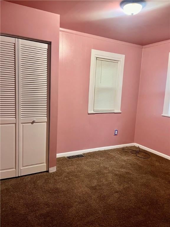 unfurnished bedroom with baseboards, visible vents, dark carpet, and a closet