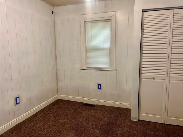 unfurnished bedroom featuring a closet, dark carpet, visible vents, and baseboards