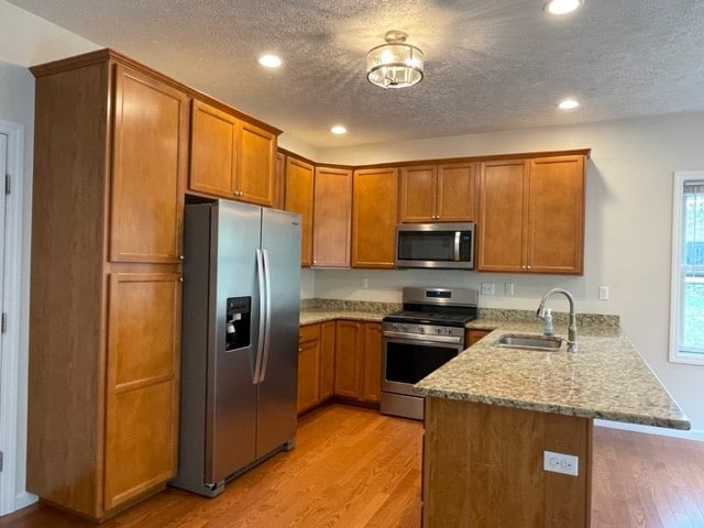 kitchen featuring a textured ceiling, kitchen peninsula, stainless steel appliances, light hardwood / wood-style floors, and sink