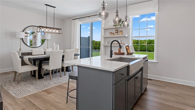 kitchen with light hardwood / wood-style flooring, stainless steel dishwasher, an island with sink, pendant lighting, and a kitchen breakfast bar