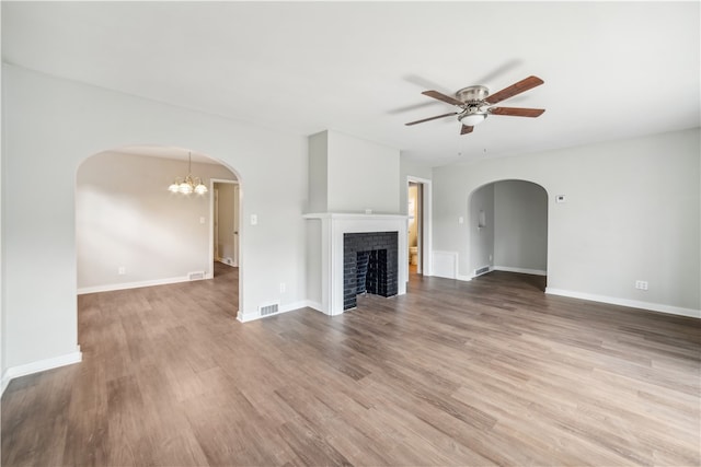 unfurnished living room featuring wood-type flooring, a fireplace, and ceiling fan with notable chandelier