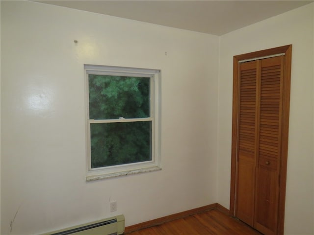 unfurnished bedroom featuring a baseboard heating unit, a closet, and hardwood / wood-style flooring