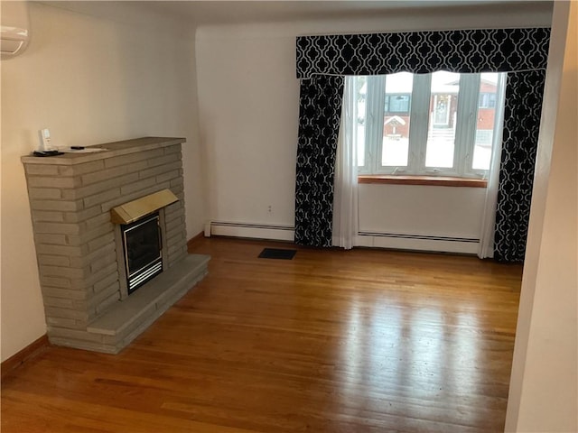 unfurnished living room featuring a wall mounted AC, light wood-type flooring, and a baseboard heating unit