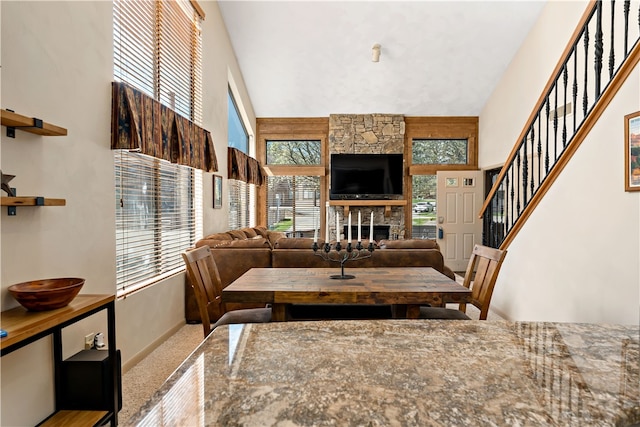 dining area with a stone fireplace, a towering ceiling, and carpet