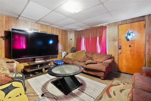 living room with wood walls, a paneled ceiling, and carpet flooring